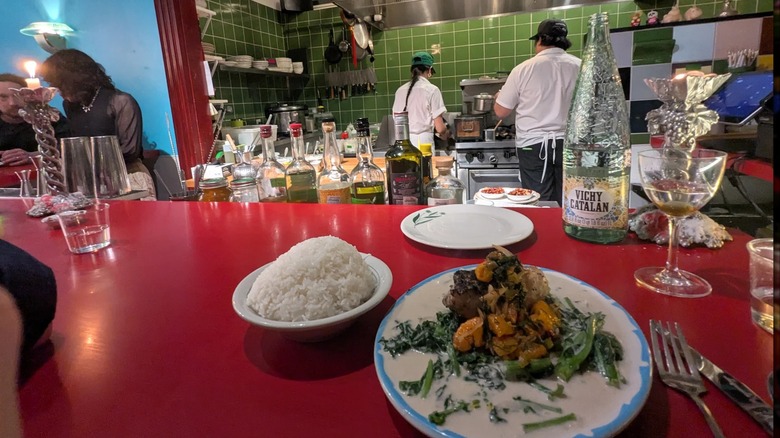 A plate of food on the red countertop with the chefs beyond working in open kitchen at Neng Jr.'s in Asheville, North Carolina