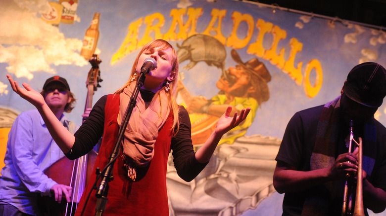 A jazz singer sings onstage with a double bassist and trumpet player at Armadillo Christmas Bazaar