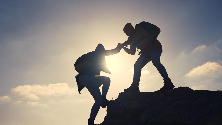 one person helping another climb over a rock