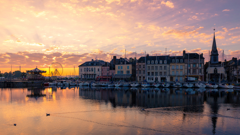 The shoreline of Deauville in France with colorful buildings, boats, and a fairground in the distance at sunset