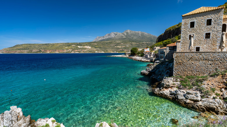 Seaside houses overlooking a cerulean sea with mountains in the background in Limeni, Greece