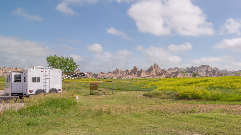 A white RV camping next to a vast field of green grass and rock outcroppings at Cedar Pass Campground, in Badlands National Park.