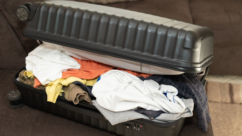 A black suitcase open and oberstuffed with clothes.