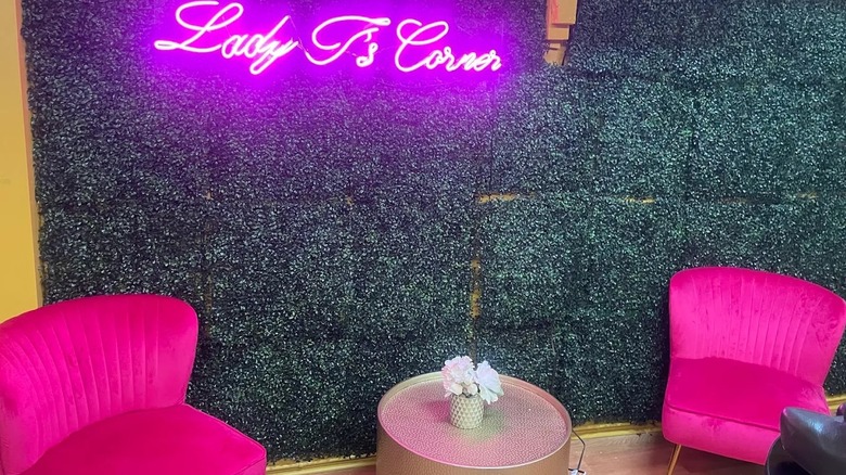 A cozy corner inside a boutique near Baltimore, with a pink neon sign, decorative grass wall and 2 pink chairs..