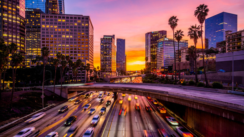 Downtown Los Angeles traffic at sunset, tall buildings surrounding a freeway with the sky in shades of pink, purple, gold and blue
