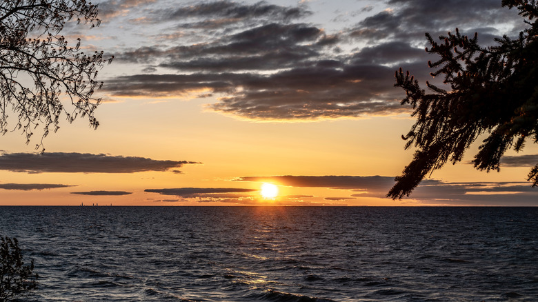 A bright orange sunset with gray clouds over Lake Michigan as viewed from a shore.