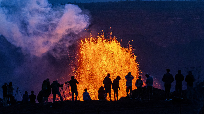 Silhouettes of people watching bright lava at night in Hawaii