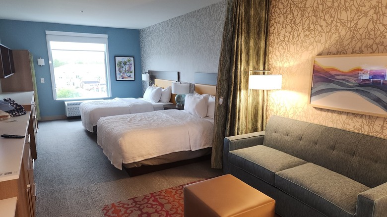 Interior view of studio-style suite at Home2 Suites by Hilton Santa Rosa Beach with curtain between two beds and living area with sofa, and soft task lighting