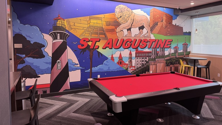 View of brightly colored "St. Augustine" mural featuring local landmarks behind a pool table in the lobby of Tru by Hilton St. Augustine I-95