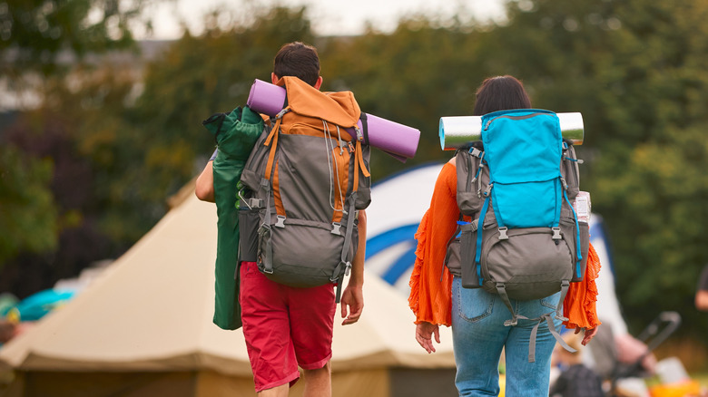 A couple carrying camping gear, walking into a music festival