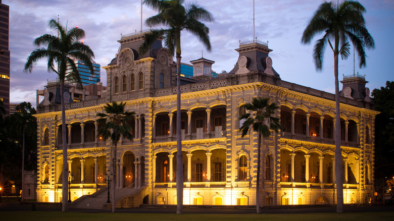 The front and side of Iolani Palace illuminated at night