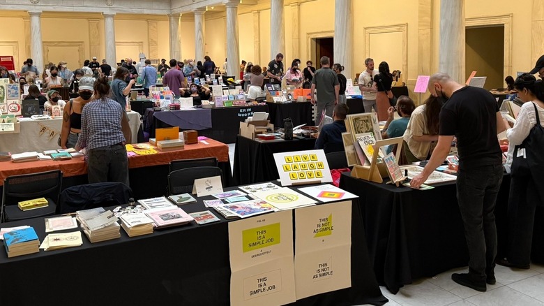Pittsburgh Art Book Fair, with people milling around black-clothed tables in rows, with white marble columns around the outer edge