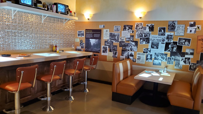 Writer's Landscape exhibit at the August Wilson Center, with orange stools at a counter along the left and an orange booth on teh right in front of a wall of black-and-white photos