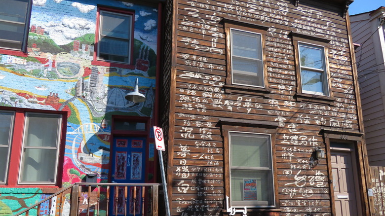 Two of the House Publications, with a colorful mural on the house on the left and a brown house on the right with white calligraphy covering it