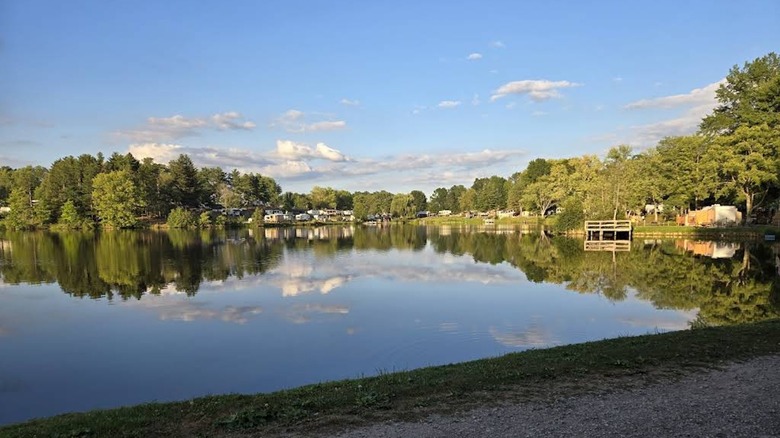 Evening light over a cloud-reflecting lake fringed by trees and a dock