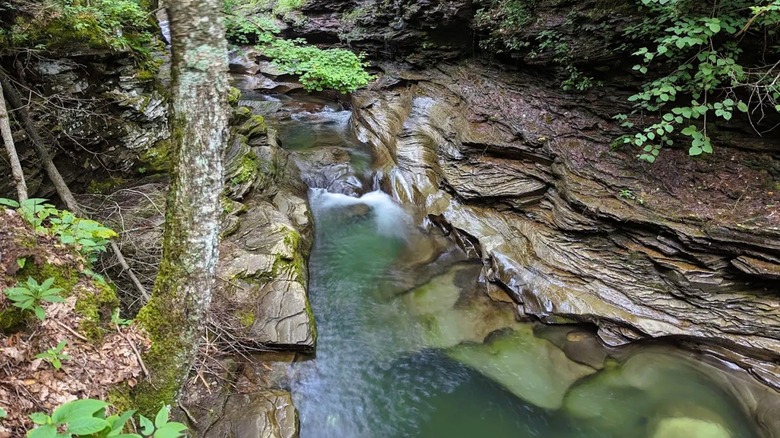 Views of a scenic area at Upper Rock Run Falls in Pennsylvania, with a flowing creek and waterfall surrounded by bedrock.