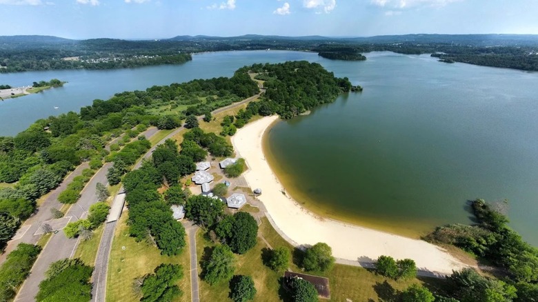 Aeriel views of Spruce Run Reservoir in New Jersey, featuring blue-green water, a large sandy shoeline, and woodlands.