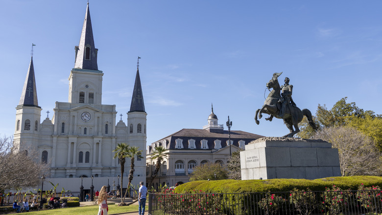 St. Louis Cathedral with pointed spires in Jackson Square in New Orleans and a horse and soldier statue in front of a blue sky and greenery