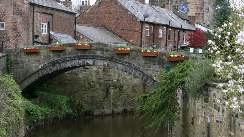 The historic stone Croston Bridge with flowers on its side over the River Yarrow in Croston, England