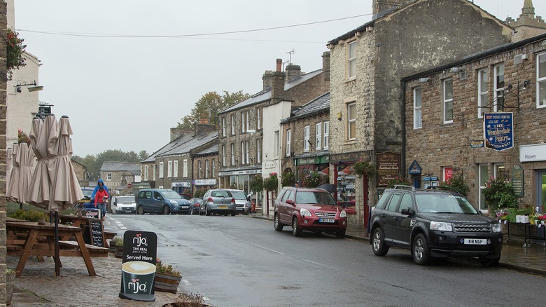Downtown Hawes with classic Brittist grey, brick buildings, pub tables on the sidewalk, and parked cars along the way