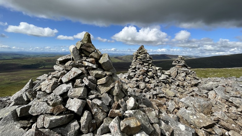 Three piles of stone arranged in round cones, with green rolling hills at Gragareth Mountain, England