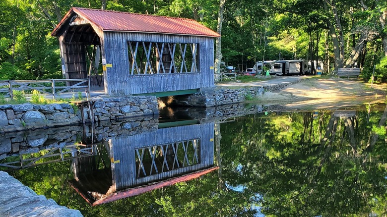 A covered bridge spans a still pond at Sutton Falls Camping Area in Massachusetts