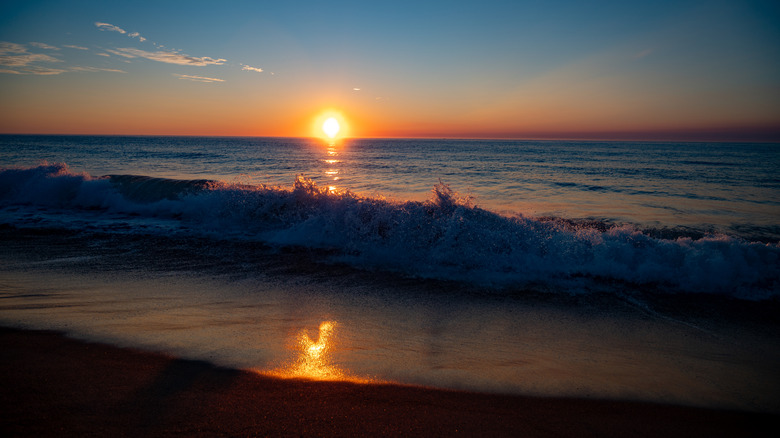 The sun setting into the horizon at Salisbury Beach, Massachusetts, with an orange reflection of the sun in the water on the beach