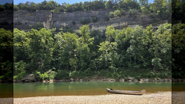 A canoe on the shore of the James River in Missouri, with forested bluffs in the background