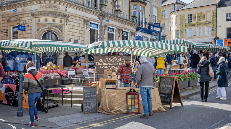 People browsing market stalls surrounded by historic buildings during a weekend market in Frome, England