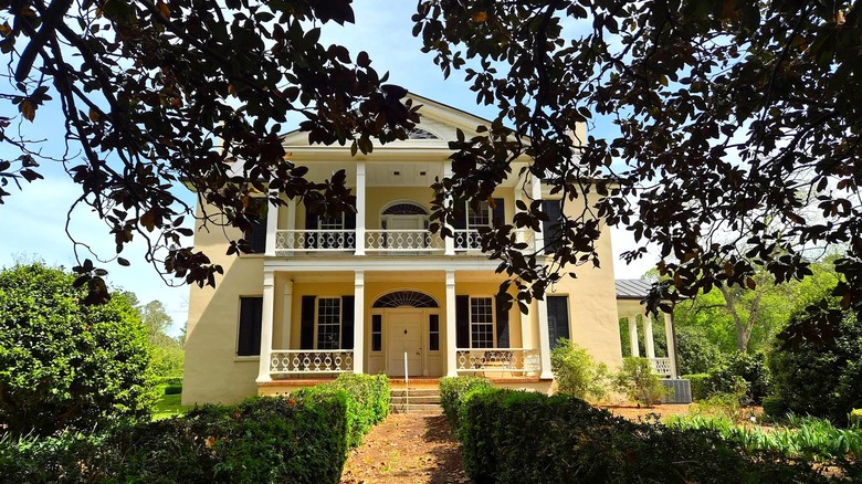 White mansion building behind shadows of trees and hedges at Rose Hill Plantation State Historic Site