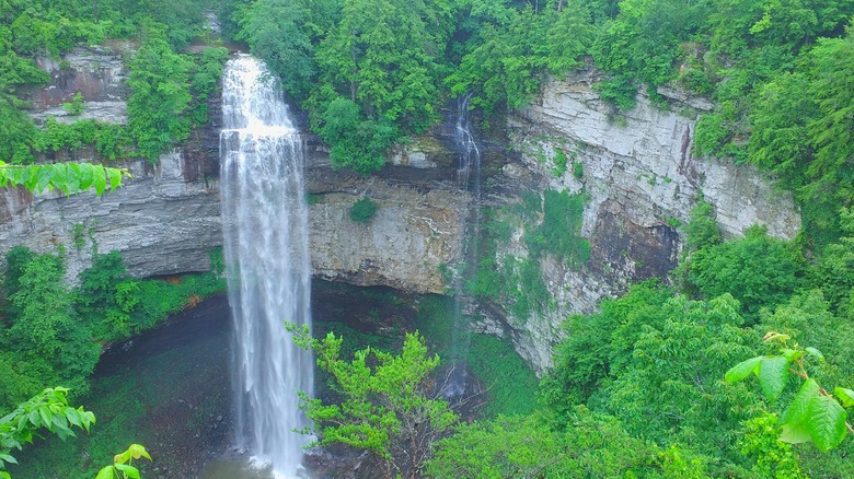 A waterfall rushes over a rock cliff into a pool surrounded by forest in Fall Creek Falls State Park near Spencer Tennessee