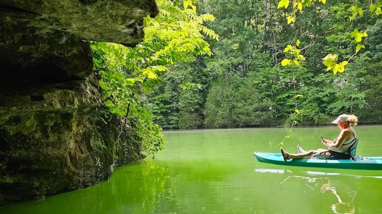 A kayaker at a cave entrance at Tims Ford Lake State Park, featuring calm, emerald water and greenery.