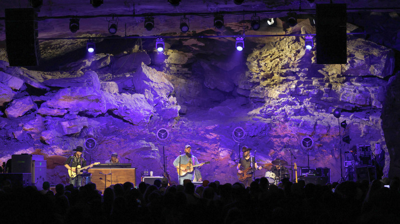 Musicians play on stage with purple-lit rocks and crowd in front in The Caverns Pelham