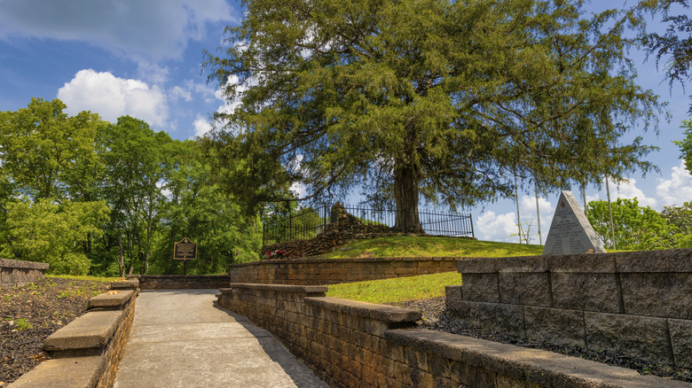 Paved path and triangular gravesite of Nancy Ward surrounded by trees in Benton, Tennessee