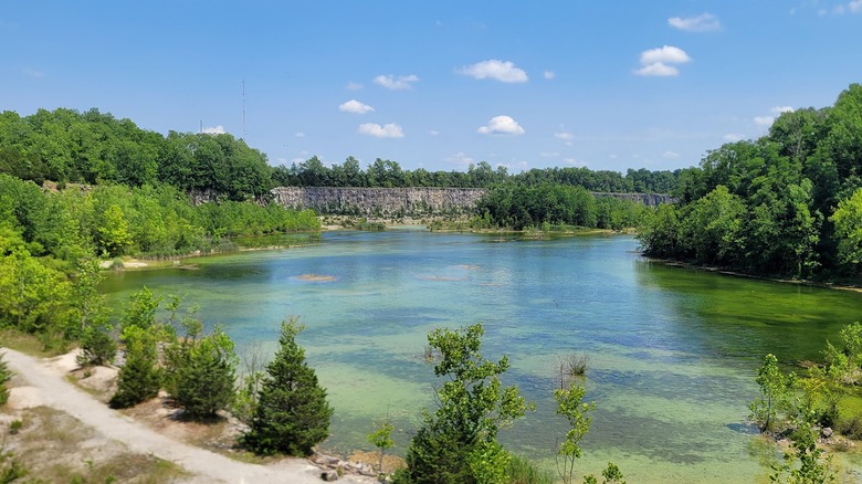 wide view of the park's lake, quarry cliff and a trail, all wooded