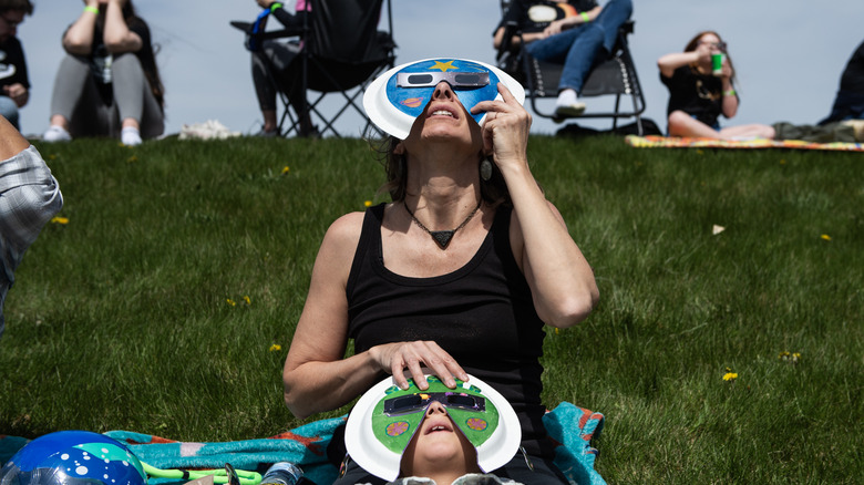 A woman and a child wearing protective glasses while looking up toward the sky