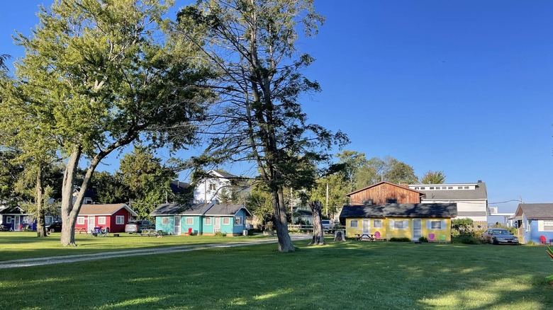 A green lawn and trees set beside colorful small beachfront cabin rentals in Mitiwanga, Ohio