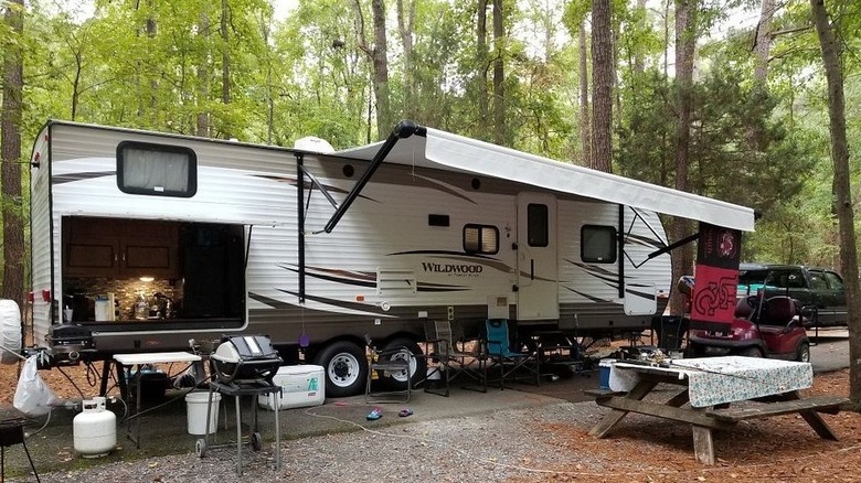 A large, white RV with an awning set up at a wooden campsite at Lake Wateree State Park.