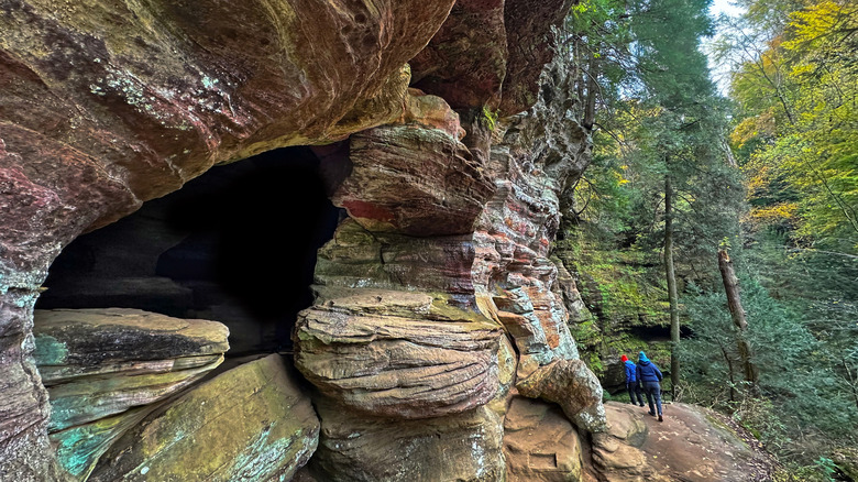 Hikers next to curved rock formation and tall trees in Hocking Hills State Park, Ohio