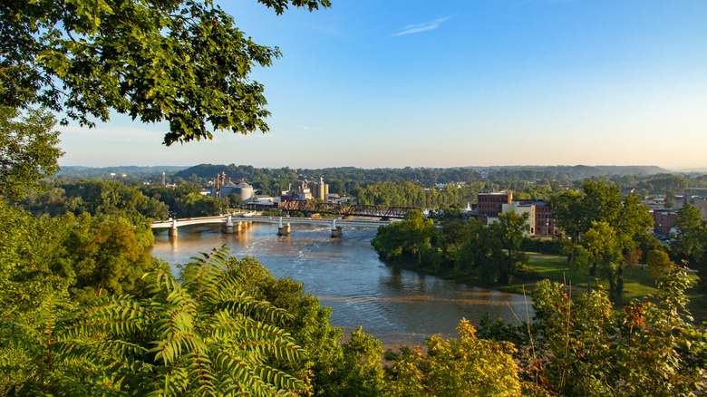 View of the Muskingum River from above, with two bridges across it and buildings to either side, and treed hills in the background under a blue sky