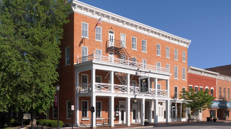 front of Golden Lamb Restaurant & Hotel, a brick building with white balconies, trees, blue sky