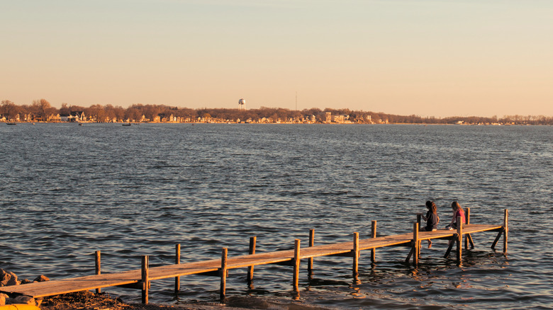 Two kids sitting on a dock at a lake