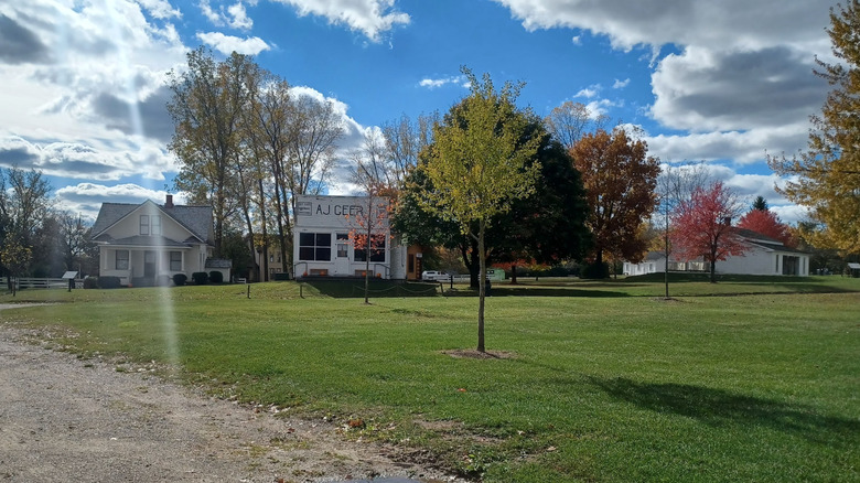 Whitepainted historic buildings behind a green lawn dotted with trees, under a cloudy blue sky
