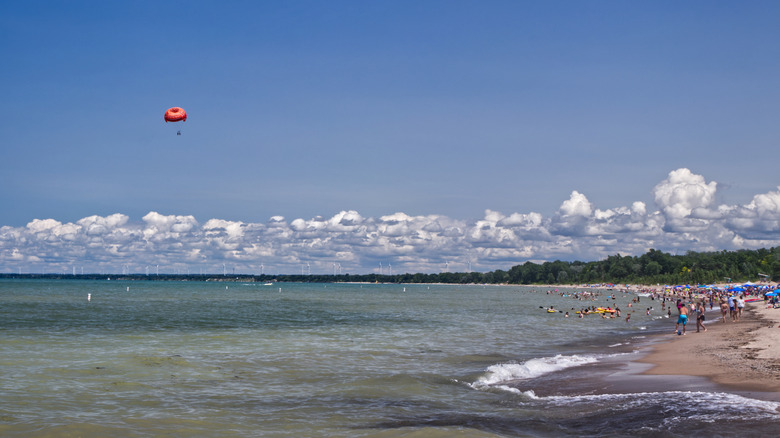 The beach in Grand Bend with clear shallow water, lots of people, a paraglider in the distance, and the Lake Huron shore