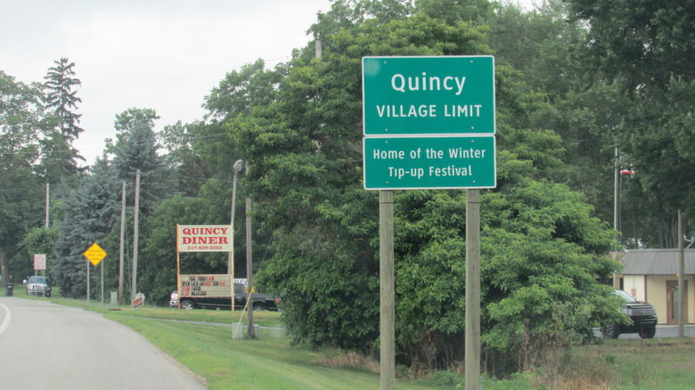 A sign reading "Quincy Village Limit: Home of the Winter Tip-Up Festival"