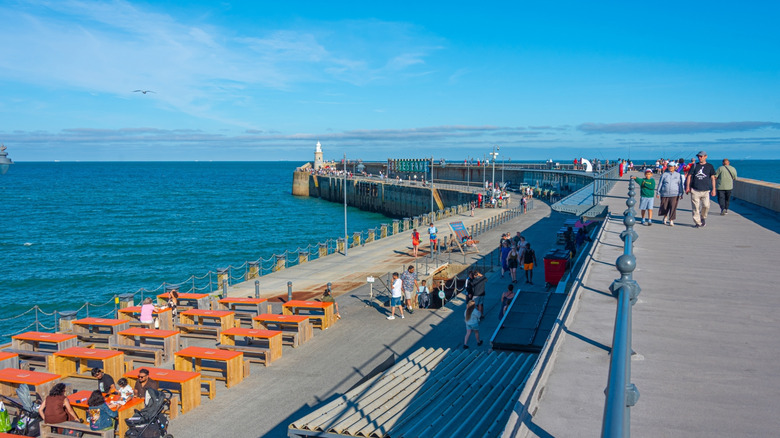 People walk on the Folkestone Harbour Arm, a jetty in the English Channel, on a sunny day
