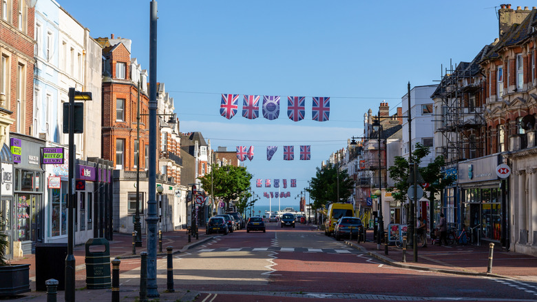 Union Jack flags strung beneath a blue sky and between shops in Bexhill-on-Sea, with the sea in the distance