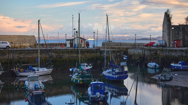 The small Dysart Harbour with fishing boats at low tide, the tall stone harbor walls around them, and the sea behind