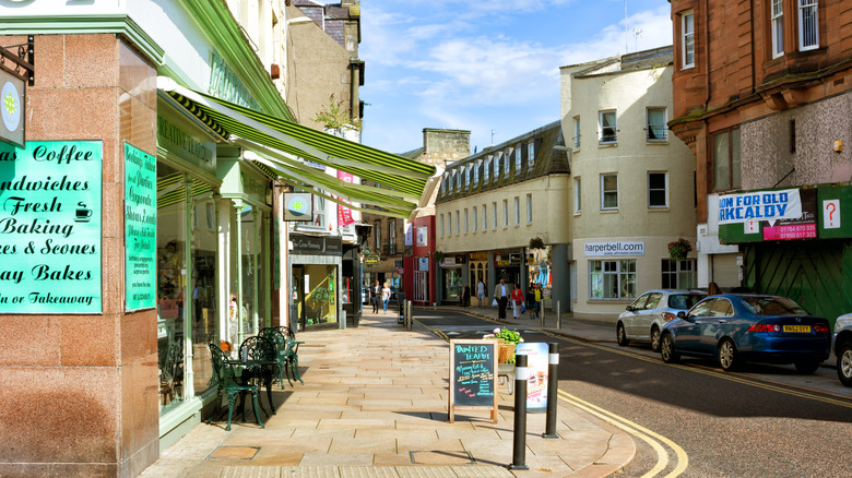 A bright street corner in downtown Kirkcaldy with a coffee shop with tables on the street and old buildings following the thin street