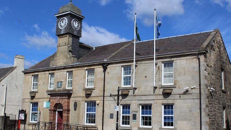 Stone building with clock tower and Scottish flags, Former Baillie Public Institute, Main Street, Whitburn